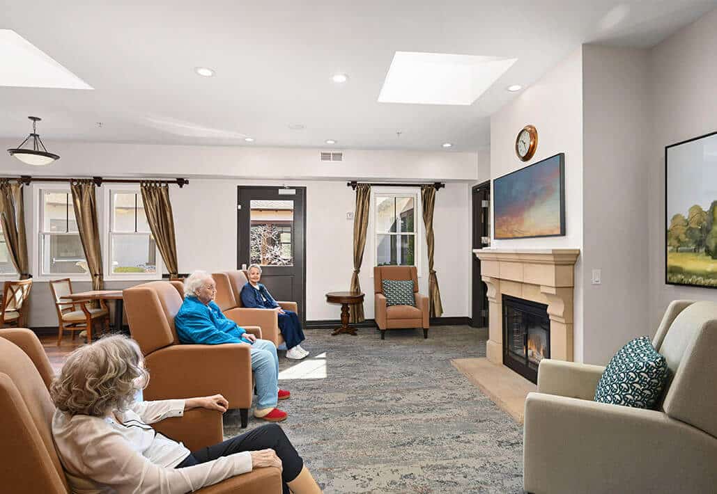 Residents gathering in a bright, cozy living room with armchairs and a fireplace.