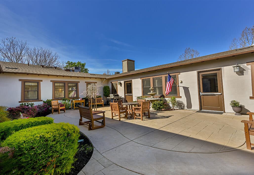 Outdoor courtyard with wooden benches and tables, decorated with plants and an American flag.