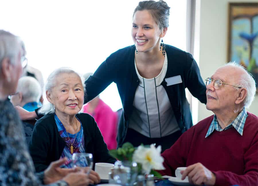 Senior living community dining room interaction between seniors and caretaker.